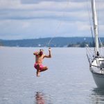 A sailor in bright pink shorts jumps off a sailboat into the water