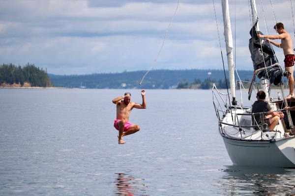 A sailor in bright pink shorts jumps off a sailboat into the water