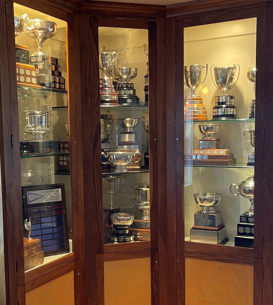 A cabinet with glass doors and wooden frame showcases a number of trophies inside. 